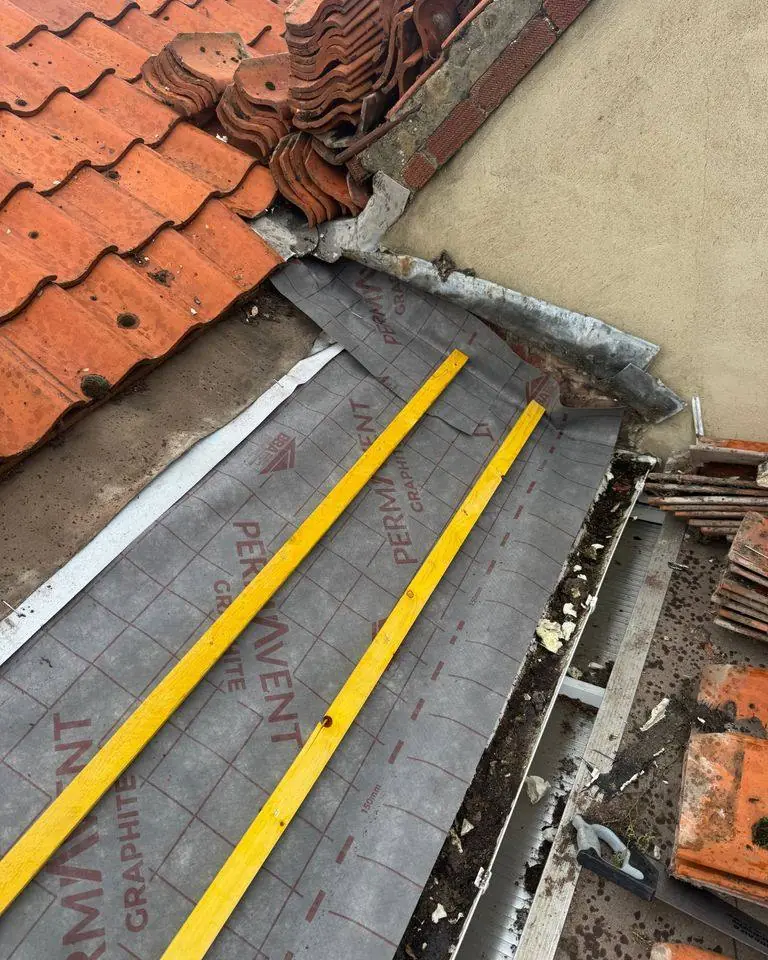 Clay pantile roof opened up at a wall abutment for new membrane, battens and lead